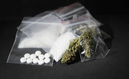 A photo of an array of leaf, powder and pill drugs in plastic bags on a black background.